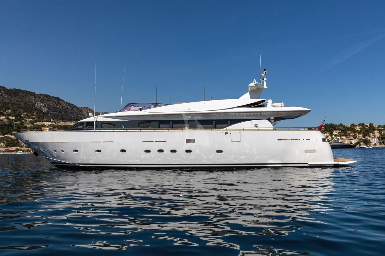A sleek, modern yacht glides gracefully on calm waters against a backdrop of coastal hills and clear blue skies. aboard TALILA Yacht for Sale