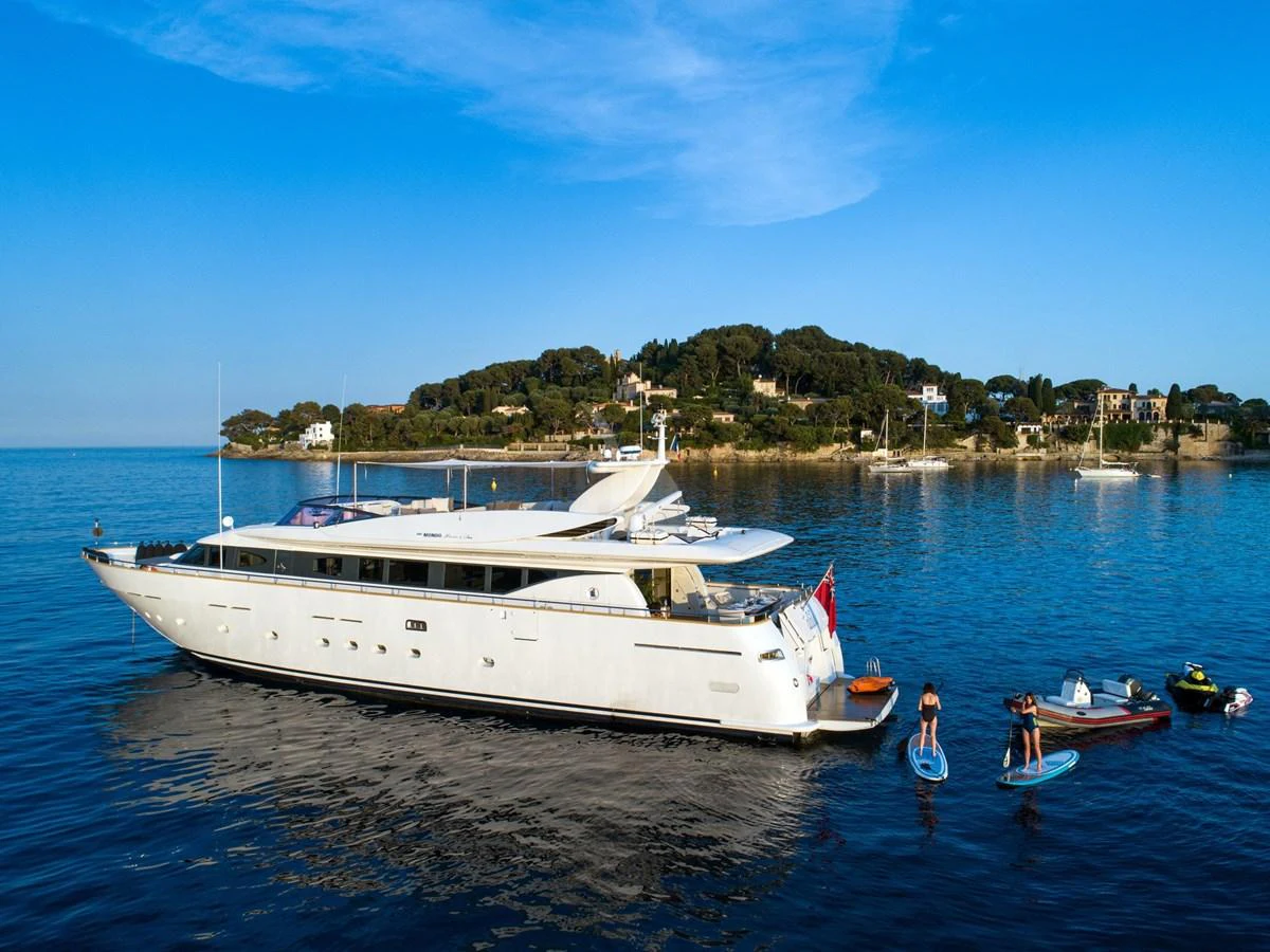 A sleek white yacht is anchored in calm waters with people enjoying water activities nearby. aboard TALILA Yacht for Sale