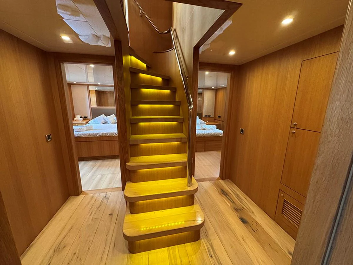 The image showcases a luxurious wooden staircase with ambient lighting, leading to a cozy and elegant interior space. aboard BANDIDO Yacht for Sale
