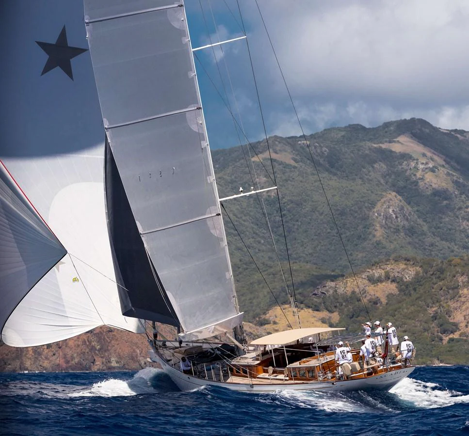 A stunning sailing yacht glides gracefully on the water with its sails fully extended against a backdrop of scenic hills. aboard ACADIA Yacht for Sale