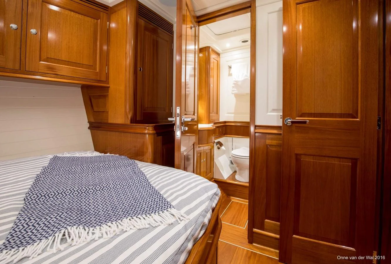 The stateroom features rich wooden cabinetry and a cozy bed with a view into the ensuite bathroom. aboard ACADIA Yacht for Sale