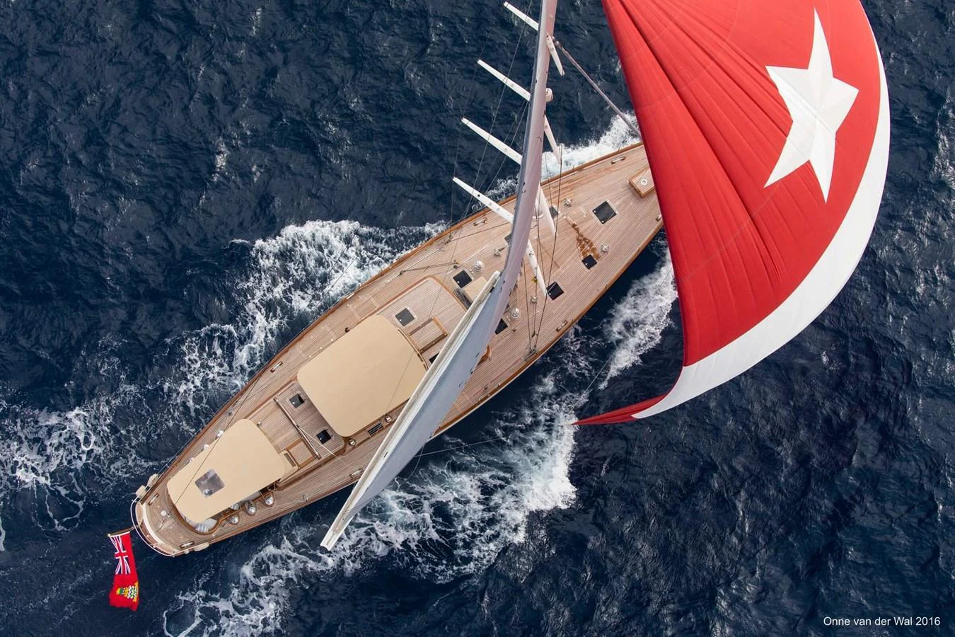 A stunning aerial view of a sailing yacht with a vibrant red sail cutting through the waves. aboard ACADIA Yacht for Sale
