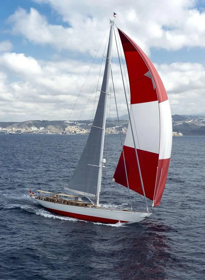 A sleek sailing yacht with a striking red and white spinnaker glides gracefully on the open sea. aboard ACADIA Yacht for Sale