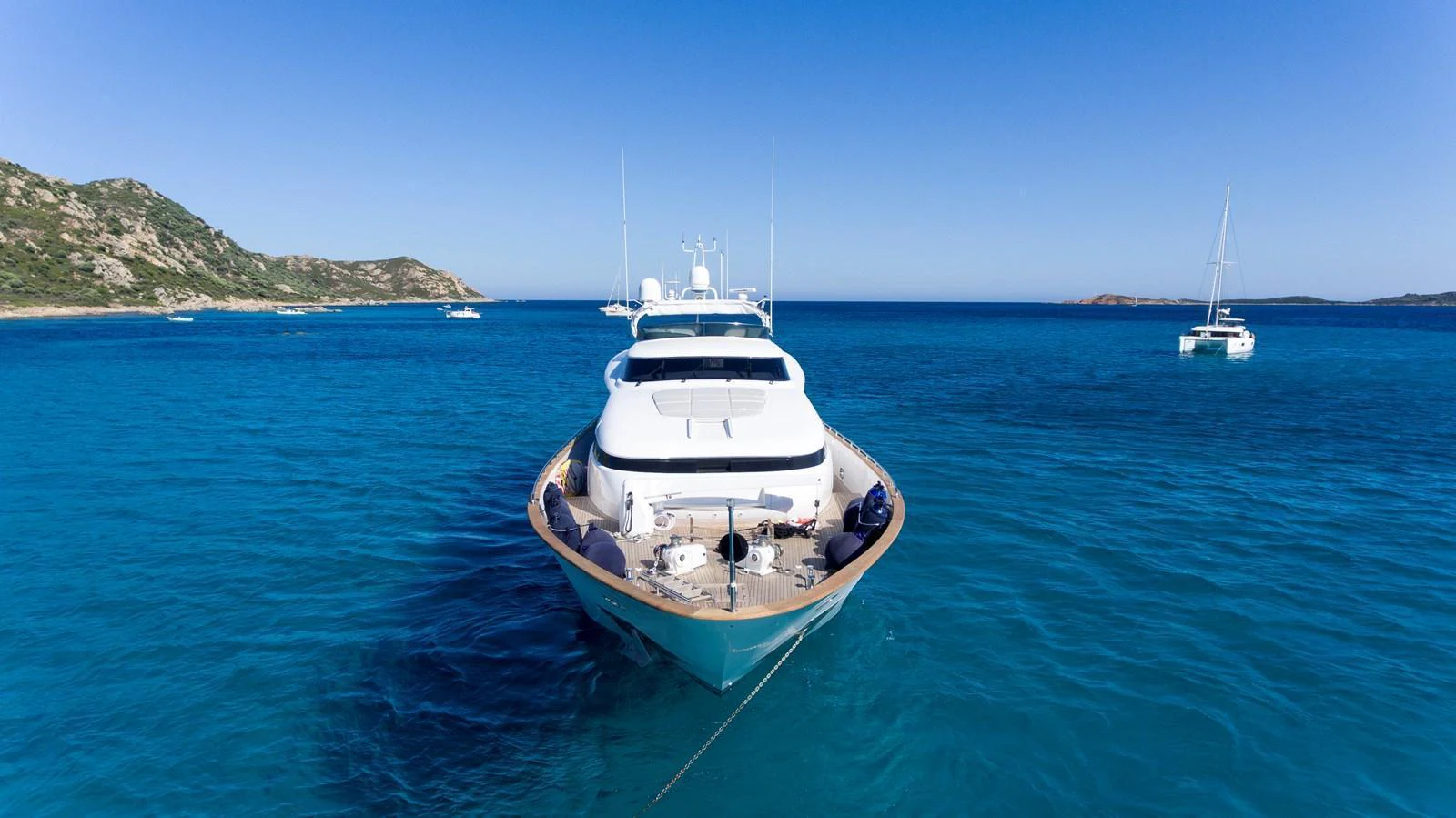 A luxurious yacht is anchored in a serene, turquoise bay with a stunning coastal backdrop. aboard AMAYA Yacht for Sale