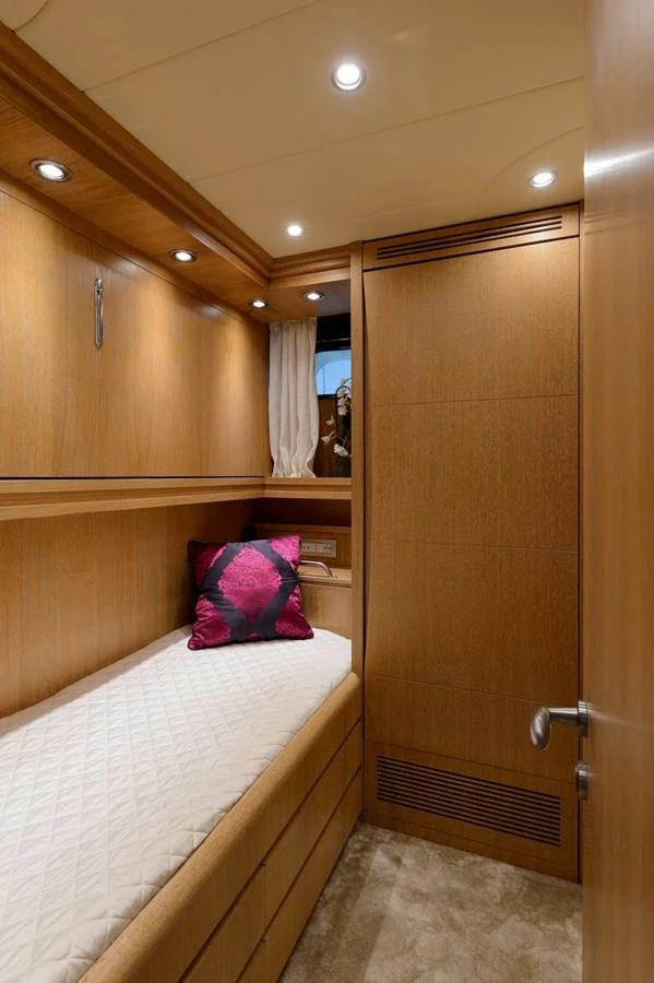 A cozy guest cabin featuring a single bed with a vibrant pillow and warm wooden finishes. aboard AMAYA Yacht for Sale