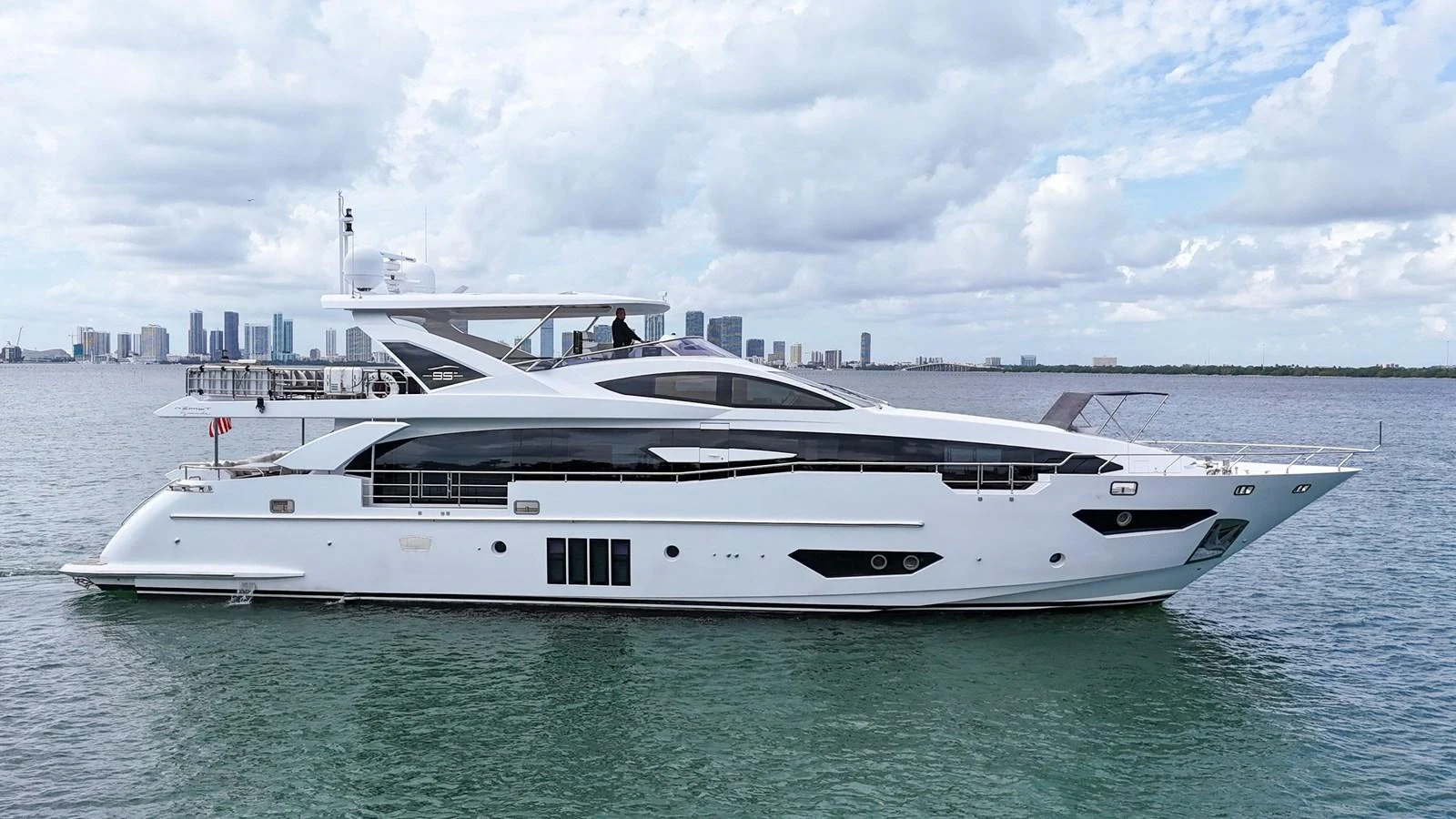 A sleek and modern yacht cruising on calm waters with a city skyline in the background. aboard 2017 AZIMUT 30 METRI Yacht for Sale
