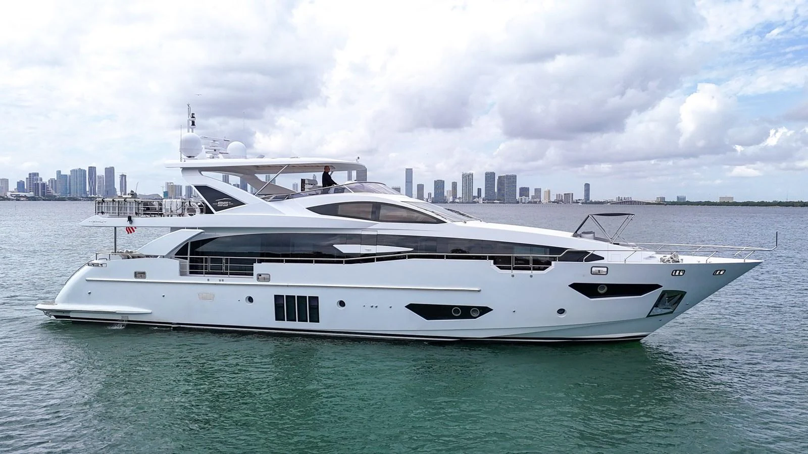 A sleek and modern yacht glides gracefully on calm waters with a city skyline in the background. aboard 2017 AZIMUT 30 METRI Yacht for Sale
