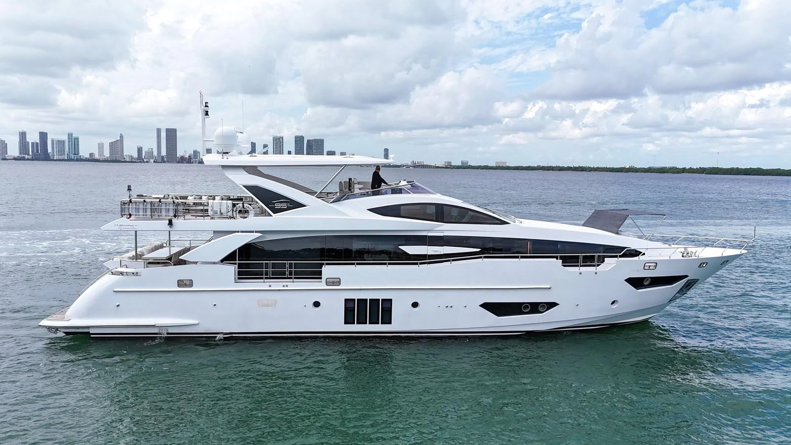 A sleek and modern yacht cruising on calm waters with a city skyline in the background. aboard 2017 AZIMUT 30 METRI Yacht for Sale