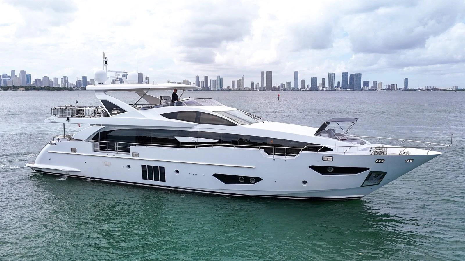 A sleek and modern yacht cruising on calm waters with a city skyline in the background. aboard 2017 AZIMUT 30 METRI Yacht for Sale