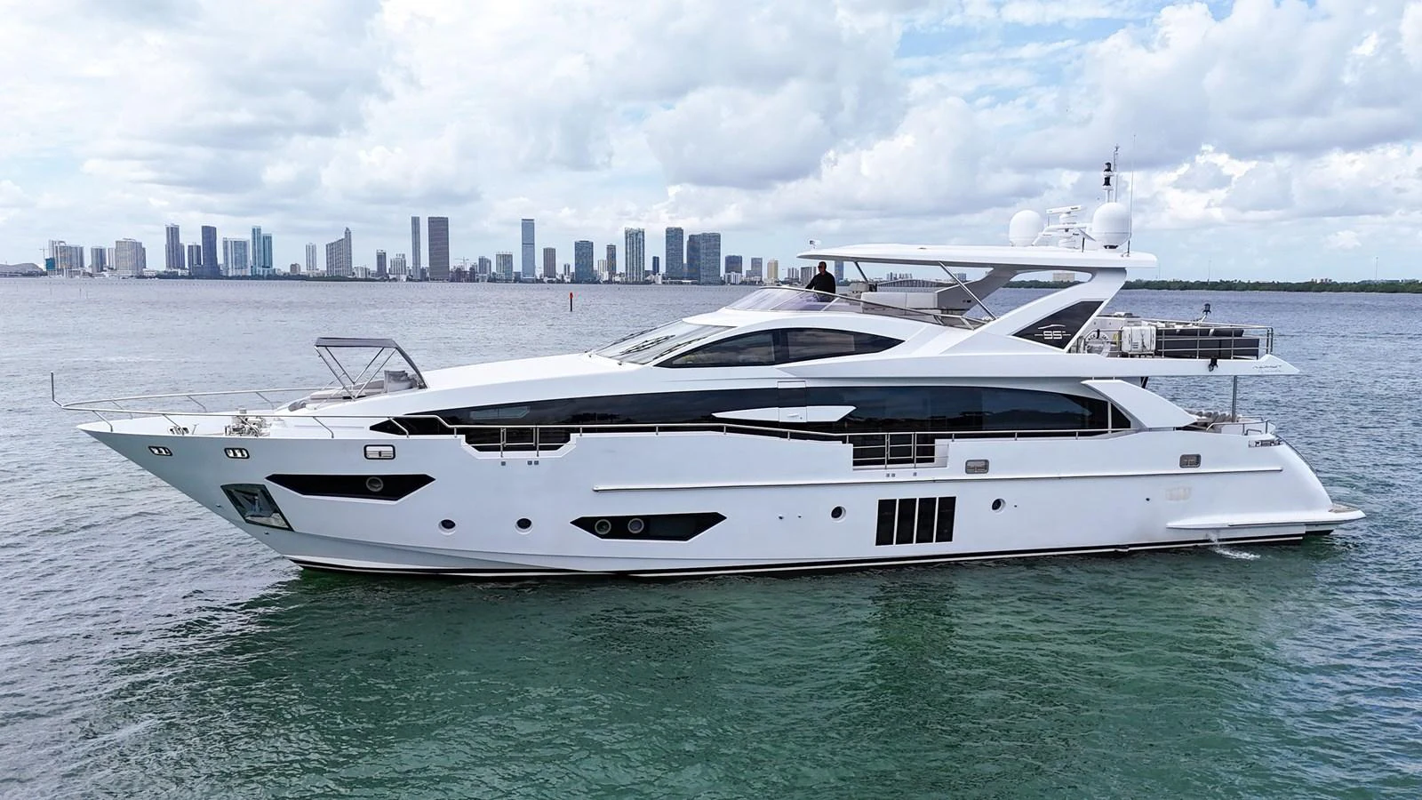 A sleek and modern yacht cruising on calm waters with a city skyline in the background. aboard 2017 AZIMUT 30 METRI Yacht for Sale