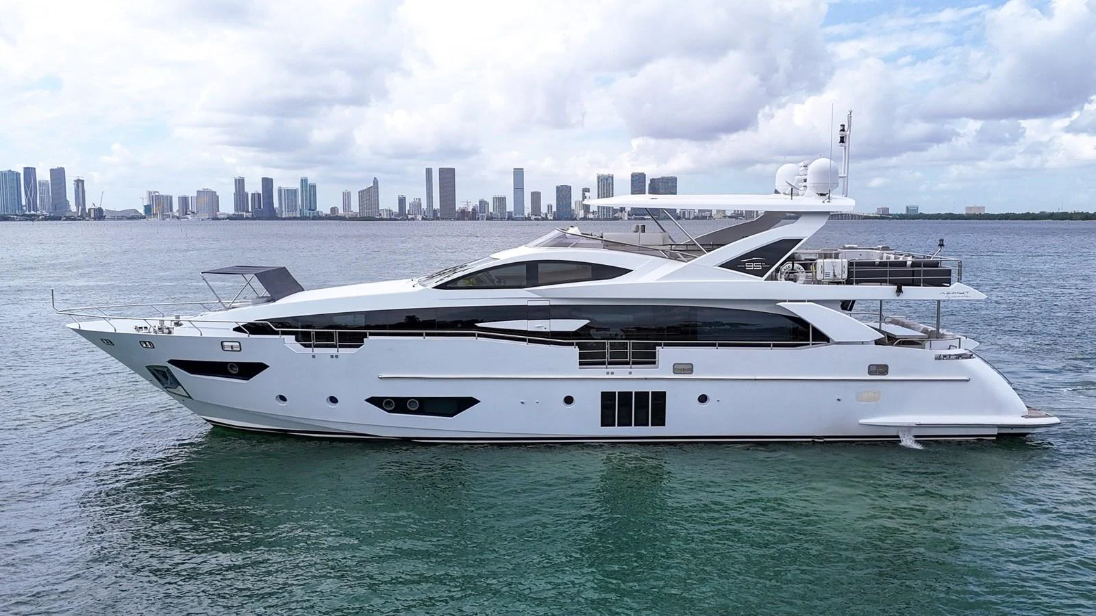 A sleek and modern yacht cruising on calm waters with a city skyline in the background. aboard 2017 AZIMUT 30 METRI Yacht for Sale