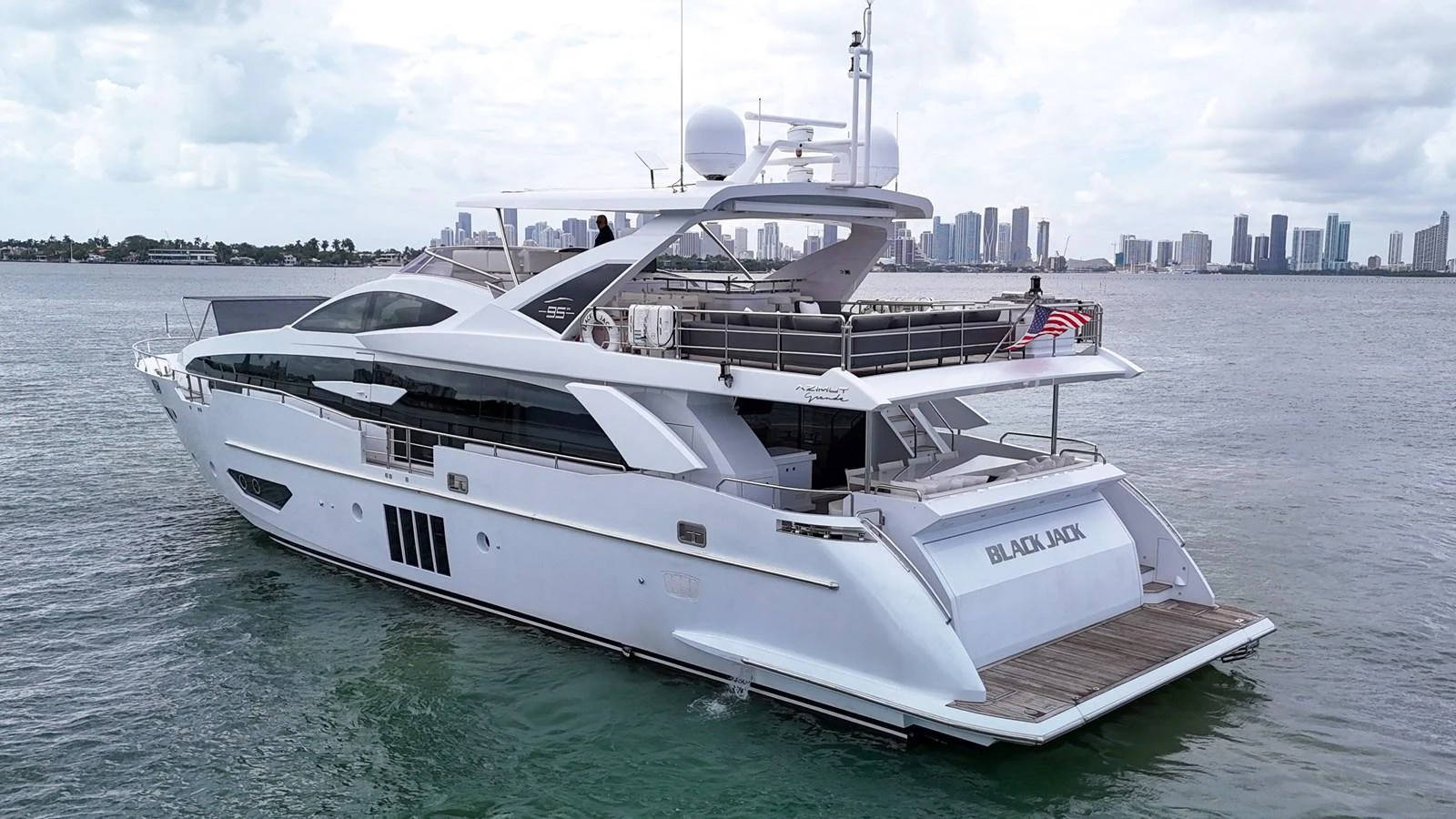 A sleek and modern yacht cruising on calm waters with a city skyline in the background. aboard 2017 AZIMUT 30 METRI Yacht for Sale