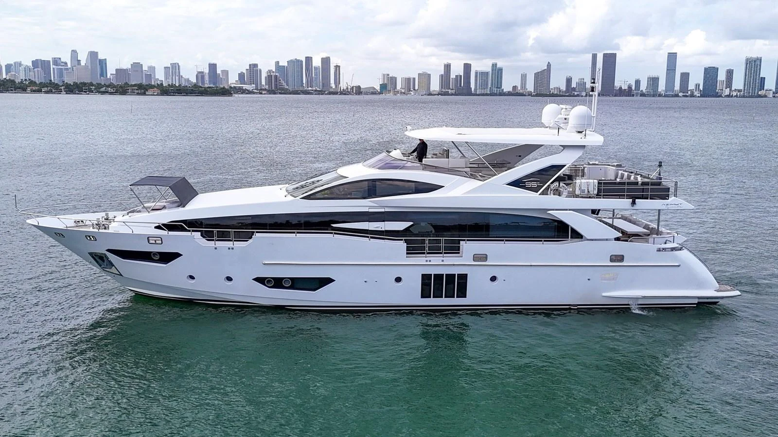 A sleek and modern yacht cruising in calm waters with a city skyline in the background. aboard 2017 AZIMUT 30 METRI Yacht for Sale