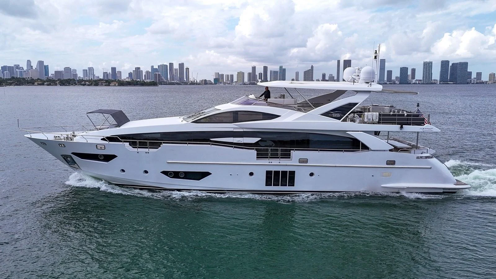 A sleek and modern yacht cruising on calm waters with a city skyline in the background. aboard 2017 AZIMUT 30 METRI Yacht for Sale