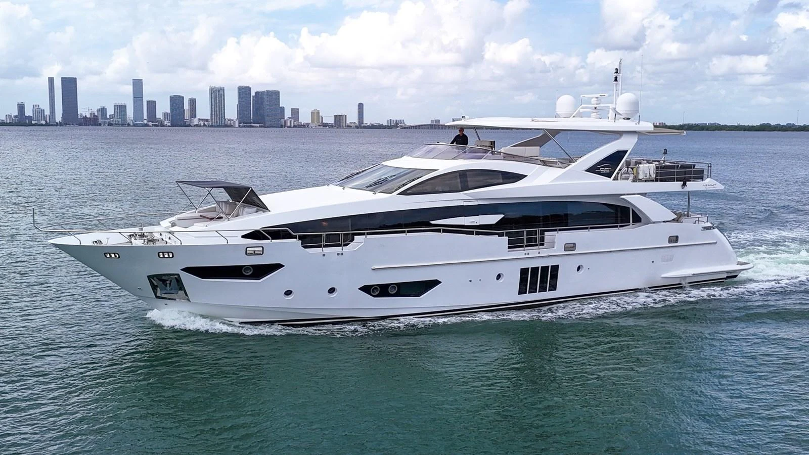 A sleek and modern yacht cruising on calm waters with a city skyline in the background. aboard 2017 AZIMUT 30 METRI Yacht for Sale
