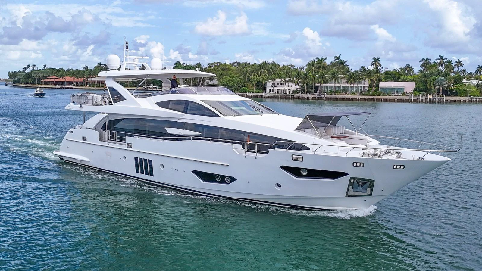 A sleek and modern yacht cruises through clear blue waters with a backdrop of lush greenery and luxurious waterfront homes. aboard 2017 AZIMUT 30 METRI Yacht for Sale
