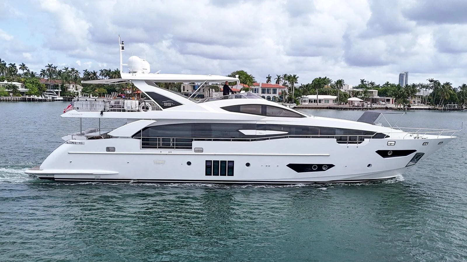 A sleek and modern yacht cruising on calm waters with a backdrop of luxurious waterfront properties. aboard 2017 AZIMUT 30 METRI Yacht for Sale