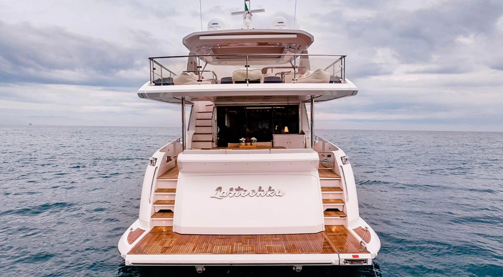 The yacht's aft deck features elegant wooden steps leading to a spacious lounging area, perfect for relaxation. aboard LASTOCHKA Yacht for Sale