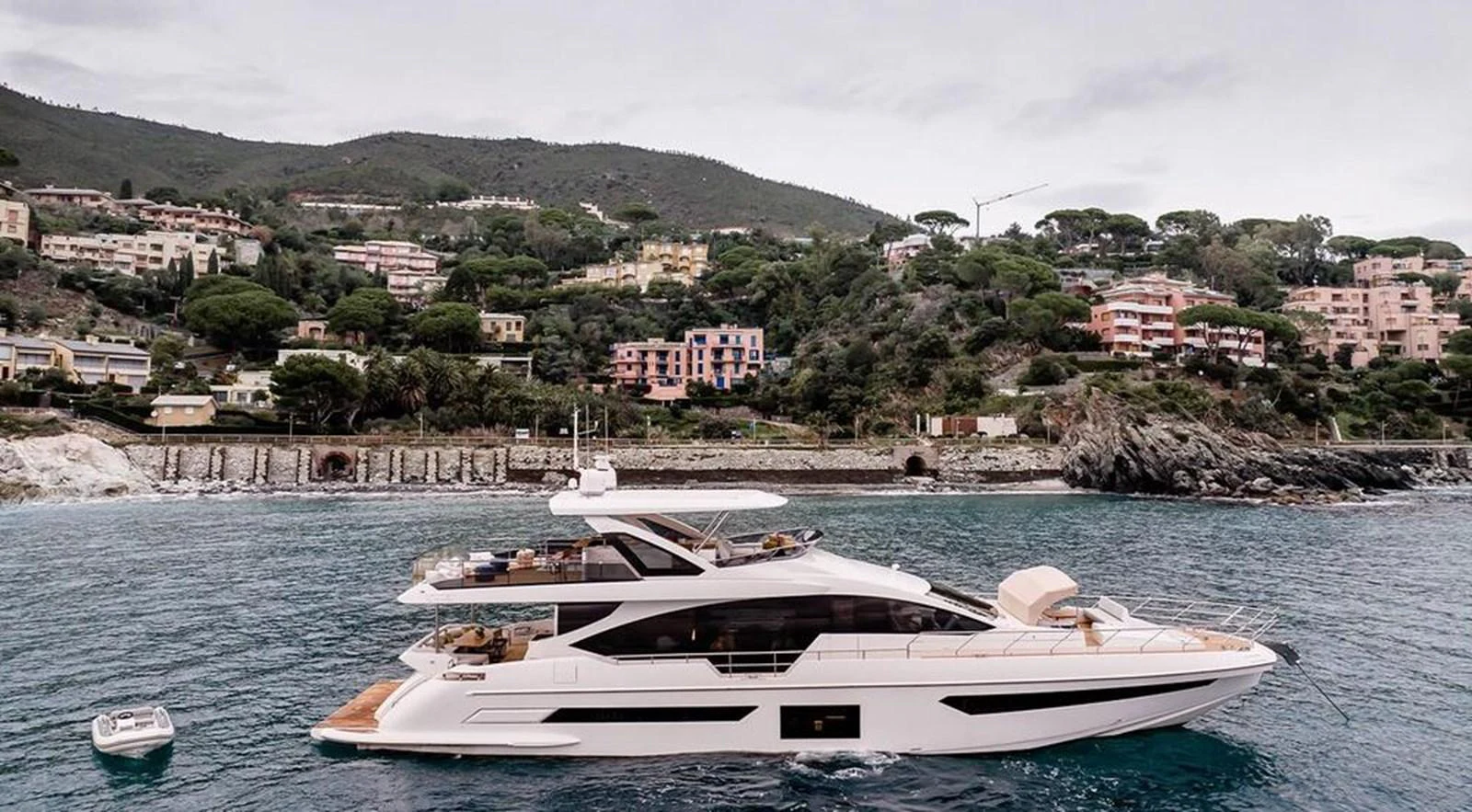 A sleek and modern yacht cruising along a picturesque coastline with lush hills and colorful buildings. aboard LASTOCHKA Yacht for Sale