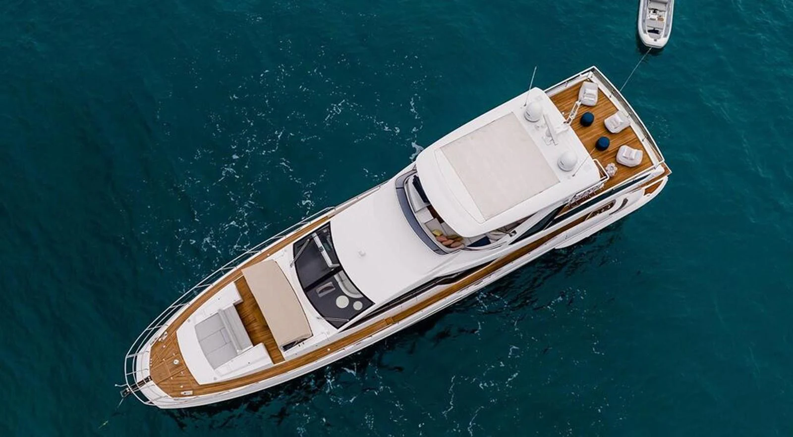 A sleek yacht with a spacious deck is seen from an aerial view, floating on clear blue waters. aboard LASTOCHKA Yacht for Sale