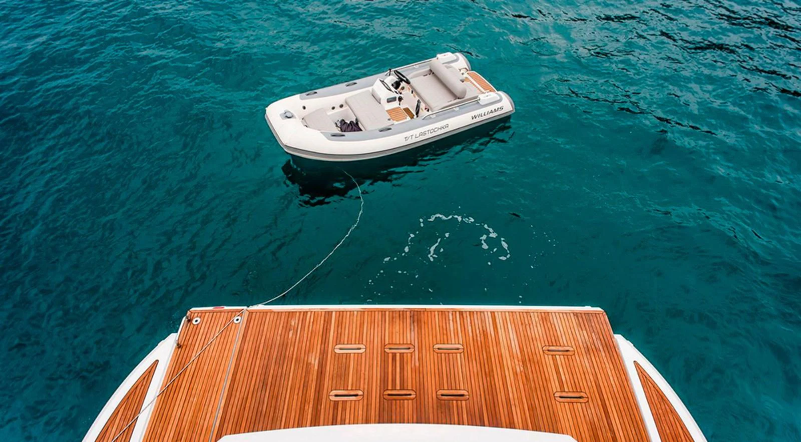 A sleek tender is tethered to the yacht, floating on clear blue waters. aboard LASTOCHKA Yacht for Sale