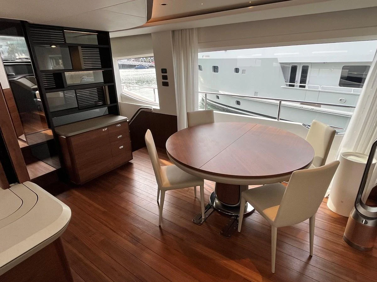 The yacht's dining area features a round wooden table with white chairs, set against large windows offering a view of the water. aboard LILYAN Yacht for Sale