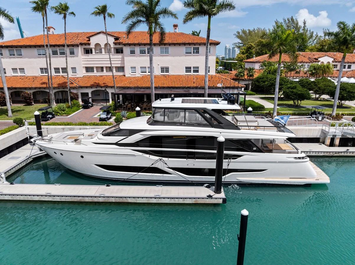 A sleek and modern yacht is docked in a picturesque marina with palm trees and Mediterranean-style buildings in the background. aboard LADY F Yacht for Sale
