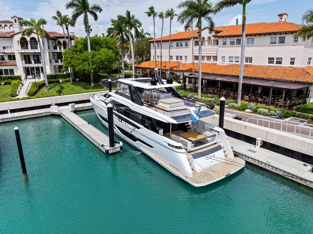A sleek yacht is docked in a serene marina with luxurious buildings in the background. aboard LADY F Yacht for Sale