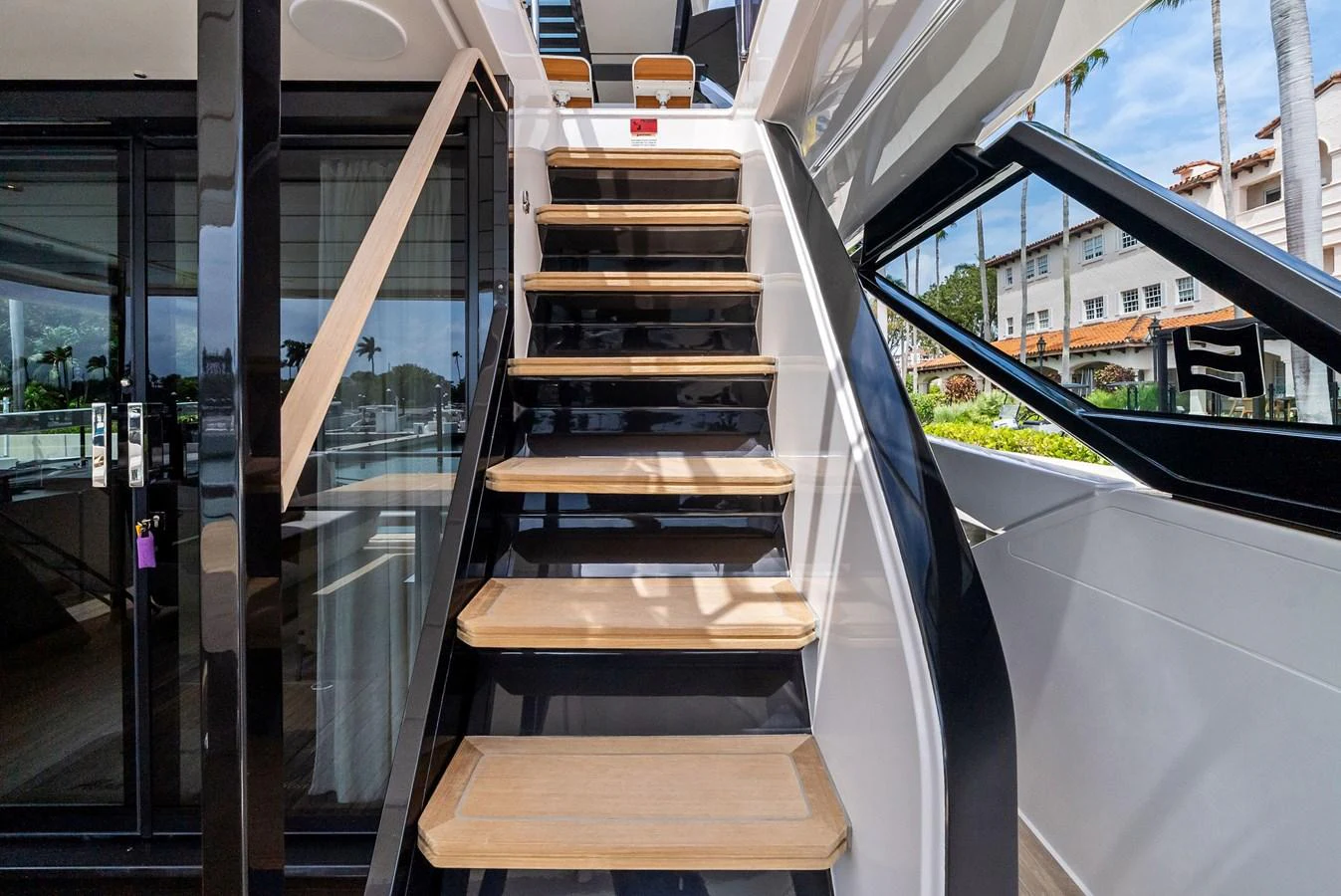 A sleek staircase with wooden steps leads to the upper deck, framed by modern glass and metal elements. aboard LADY F Yacht for Sale