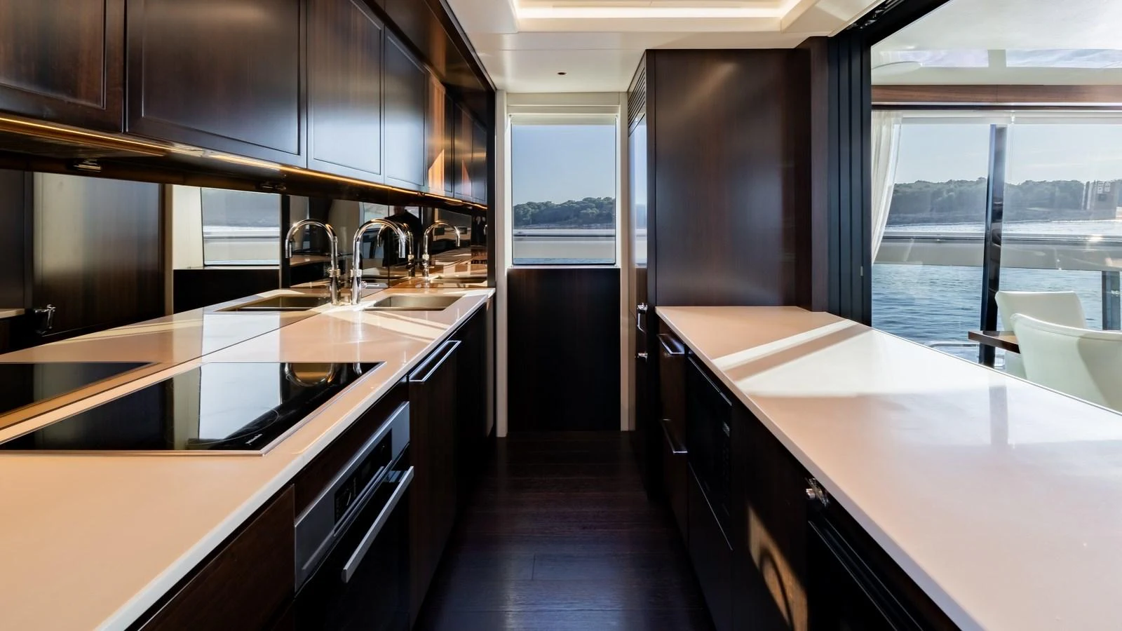 The galley features sleek dark cabinetry and modern appliances with a view of the water through large windows. aboard TRIPLE EIGHT Yacht for Sale