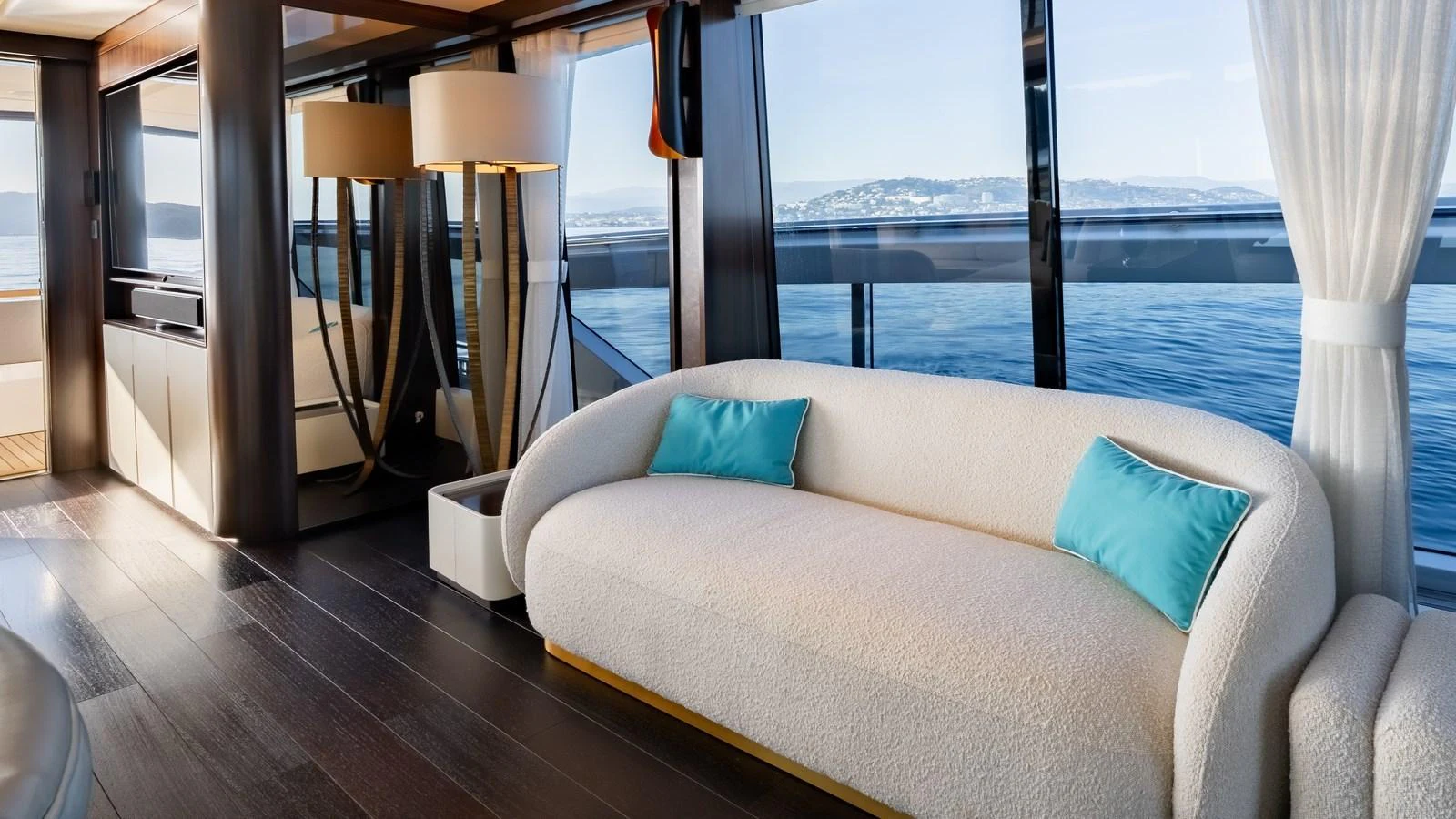 The salon features a plush white sofa with turquoise accent pillows, offering a serene view of the sea through large windows. aboard TRIPLE EIGHT Yacht for Sale