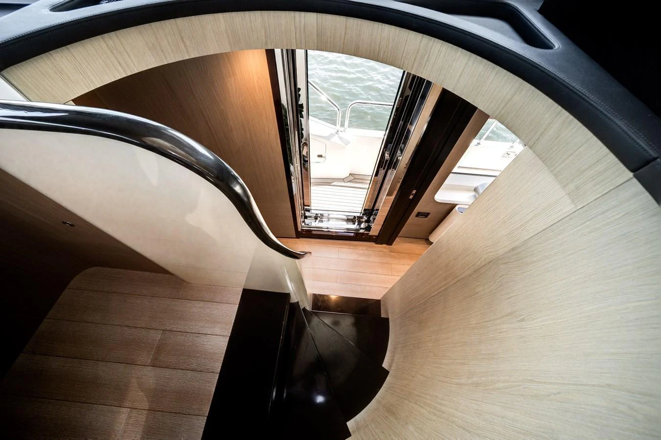 A stylish staircase with a sleek handrail leads down to the lower deck, with a view of the water through the open doors. aboard PIER PRESSURE Yacht for Sale