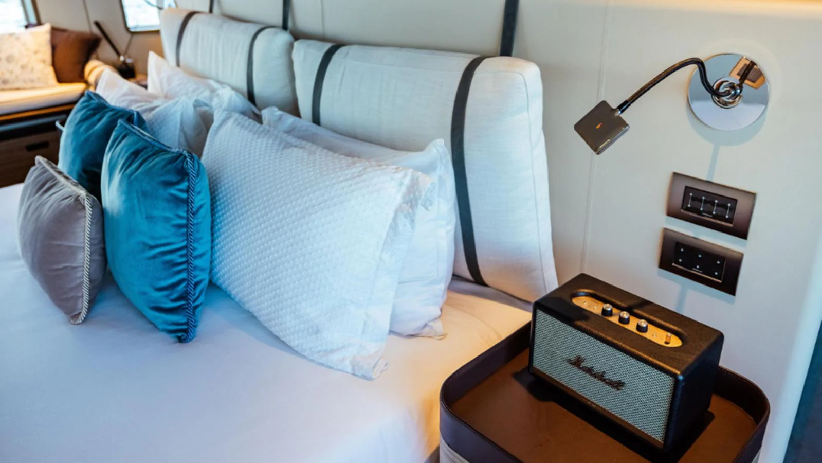 The stateroom features a luxurious bed with plush pillows and a stylish bedside table with a modern lamp and speaker. aboard MARCH SUNRISE Yacht for Sale