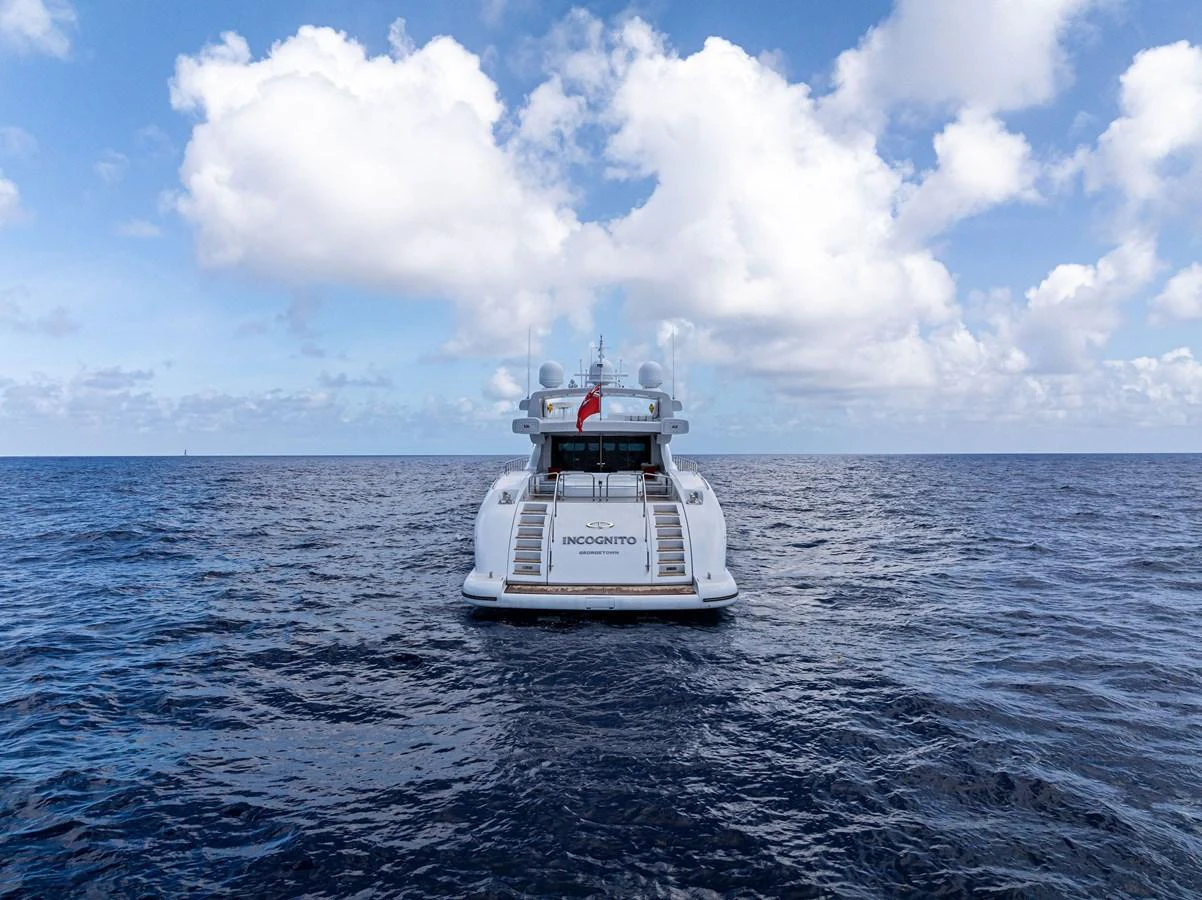 The yacht is seen from the rear, cruising on open water under a partly cloudy sky. aboard INCOGNITO Yacht for Sale