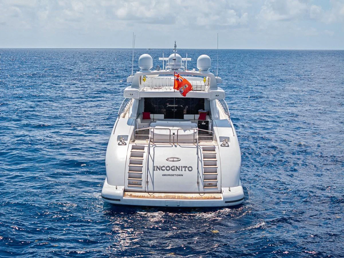 A luxurious yacht is seen from the rear, cruising on open waters under a clear sky. aboard INCOGNITO Yacht for Sale