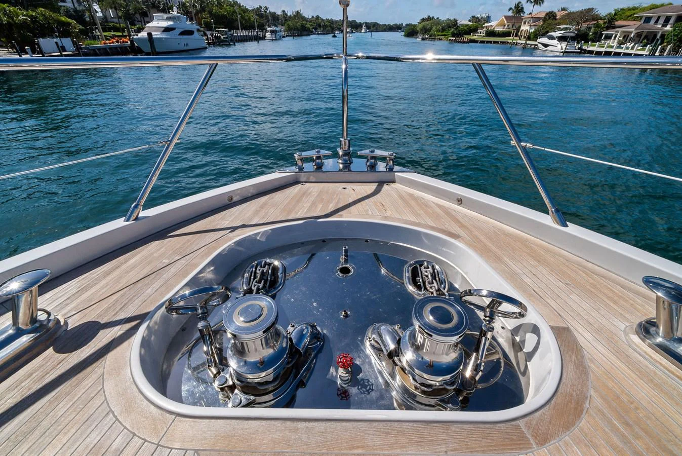 The yacht's bow features polished stainless steel winches and a teak deck, set against a serene waterfront backdrop. aboard INCOGNITO Yacht for Sale