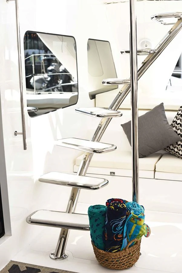 A sleek, modern staircase with polished metal steps leads to an upper deck, complemented by a cozy seating area and a basket of colorful towels. aboard SILHOUETTE 800 Yacht for Sale