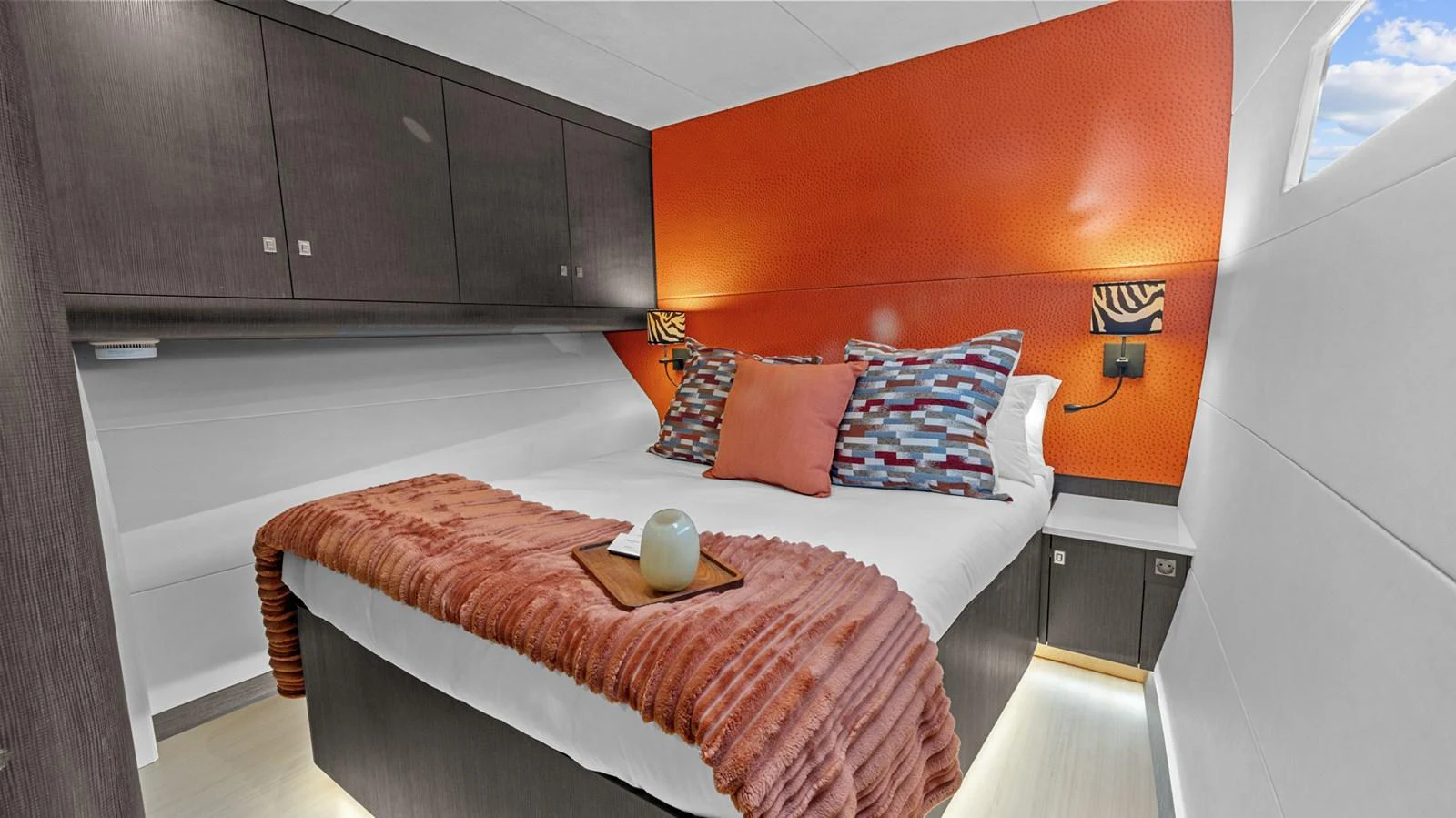 A cozy stateroom featuring a double bed with vibrant orange accents and modern cabinetry. aboard SILHOUETTE 800 Yacht for Sale