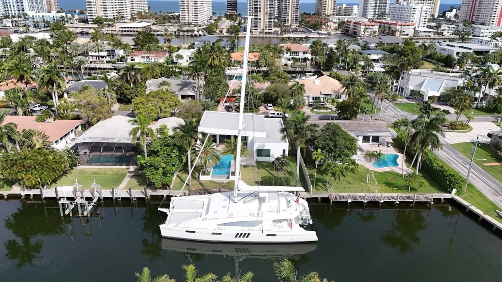 A sleek white yacht is docked in a serene canal, surrounded by lush greenery and luxurious waterfront homes. aboard SILHOUETTE 800 Yacht for Sale