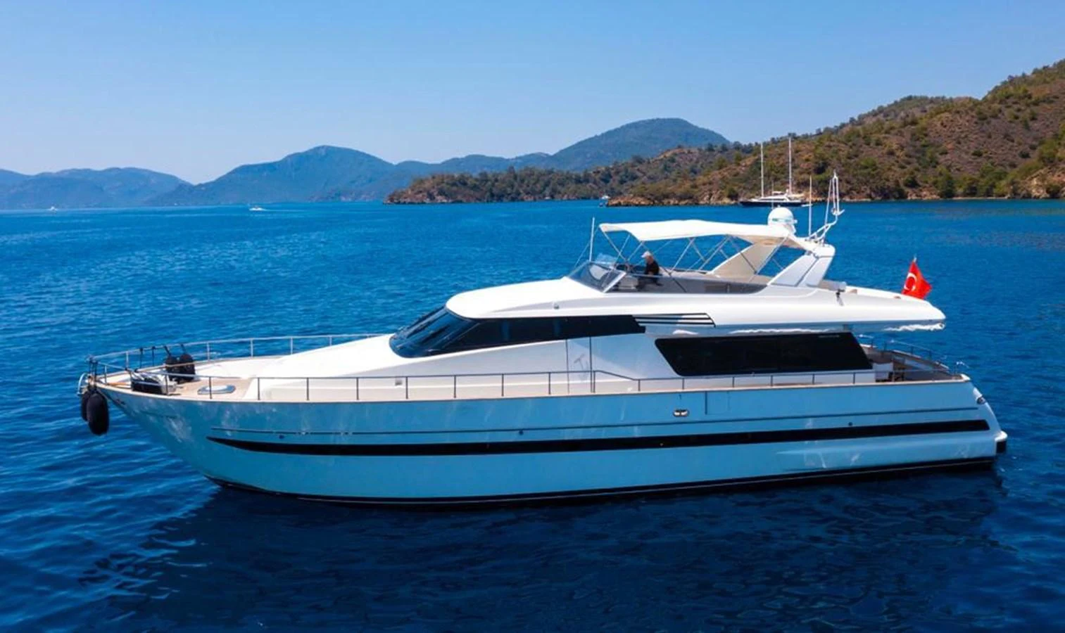 A sleek yacht glides gracefully on calm blue waters with scenic hills in the background. aboard BARBAROSSA MORATTI Yacht for Sale