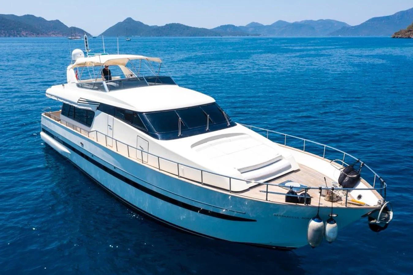 A sleek yacht glides gracefully on clear blue waters with a stunning backdrop of distant mountains. aboard BARBAROSSA MORATTI Yacht for Sale