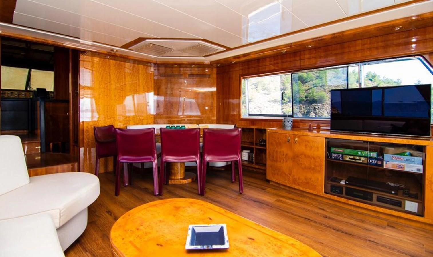 The salon features a cozy seating area with a dining table and entertainment center, bathed in natural light. aboard BARBAROSSA MORATTI Yacht for Sale