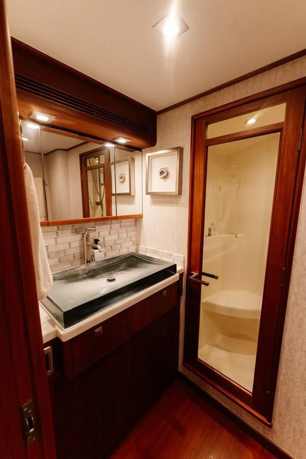 The yacht's bathroom features a sleek sink and a glass-enclosed shower. aboard NEVER SAY NEVER Yacht for Sale