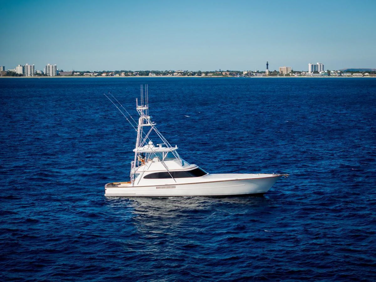 A sleek yacht cruises on calm blue waters with a cityscape in the background. aboard NEVER SAY NEVER Yacht for Sale