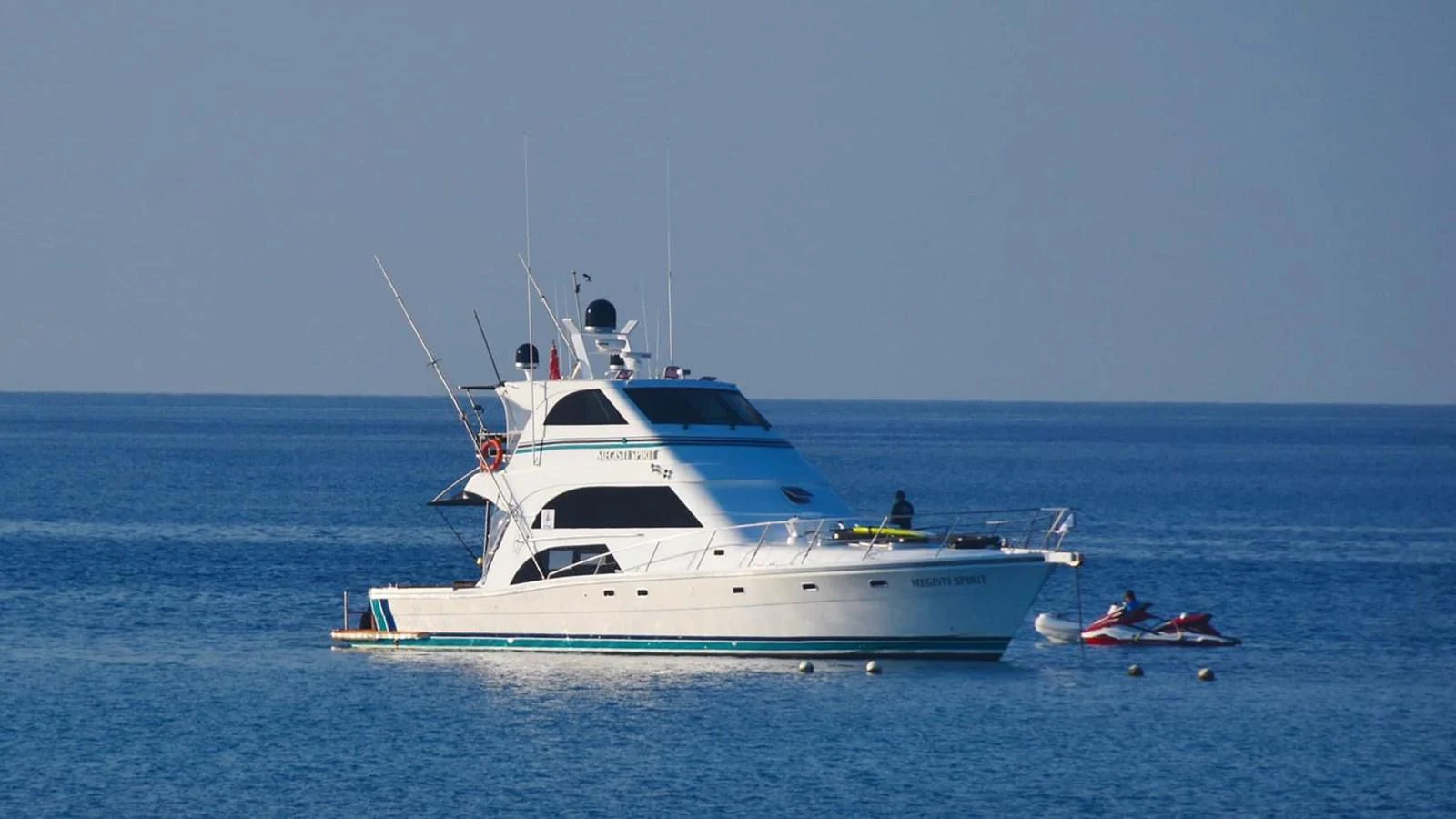 A sleek yacht is anchored on calm blue waters, with a jet ski nearby. aboard MEGISTI SPIRIT Yacht for Sale