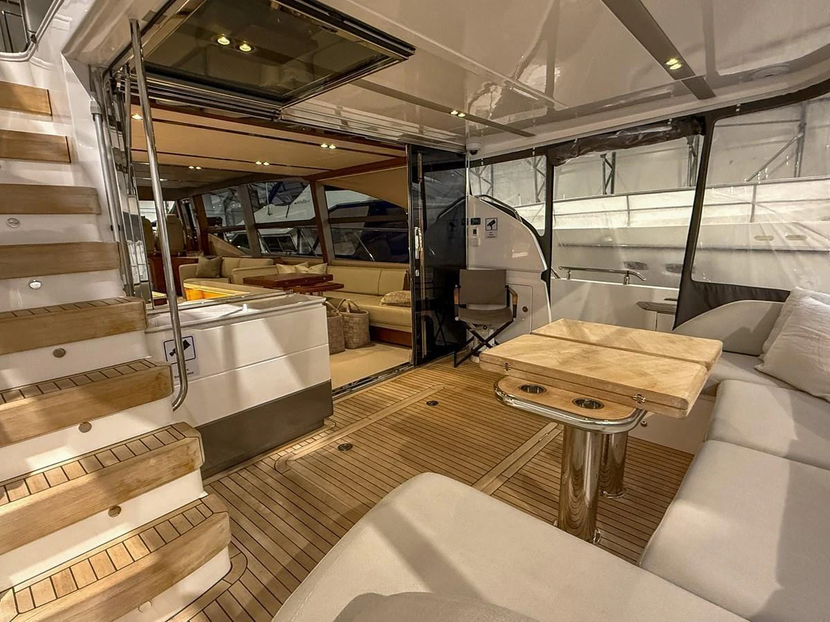The aft deck features a luxurious seating area with a wooden table, seamlessly connecting to the interior living space. aboard PRINCESS 70 Yacht for Sale