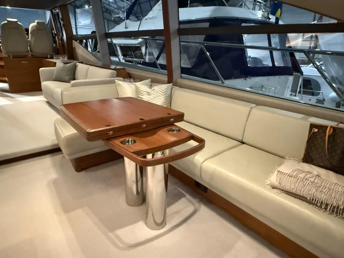 The salon features a comfortable seating area with a wooden table and large windows offering a view of the marina. aboard PRINCESS 70 Yacht for Sale
