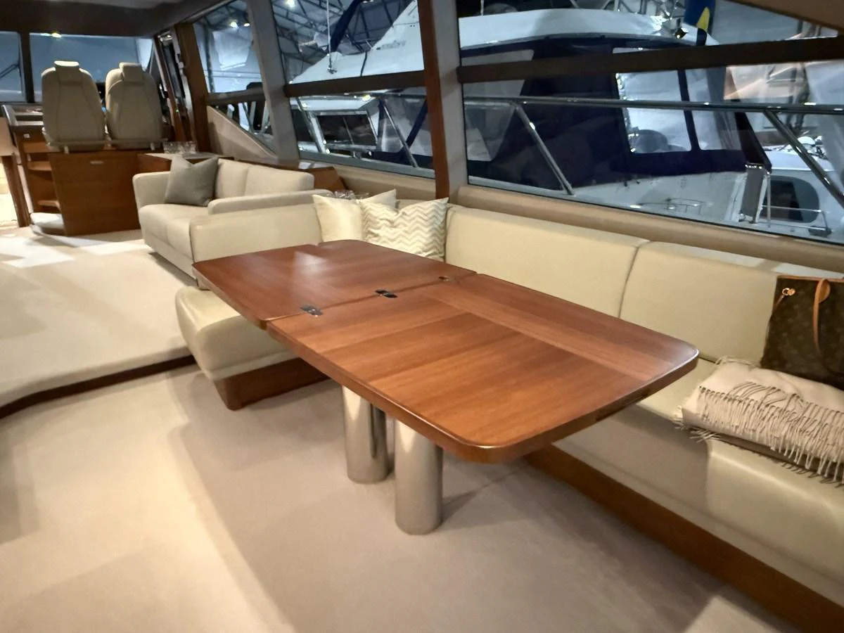 The salon features a comfortable seating area with a wooden table and large windows offering a view of the marina. aboard PRINCESS 70 Yacht for Sale