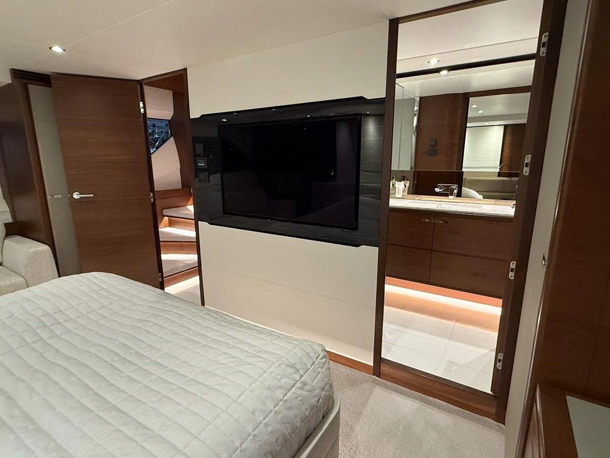 The stateroom features a comfortable bed, a flat-screen TV, and a view into a modern en-suite bathroom. aboard PRINCESS 70 Yacht for Sale