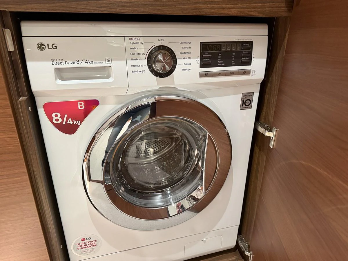 The image shows a washing machine installed within a wooden cabinet on the yacht. aboard PRINCESS 70 Yacht for Sale